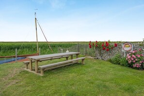 Ein Picknickbereich mit Tisch und Bänken, eine Steinmauer mit einem Schild und ein grünes Feld im Hintergrund.
