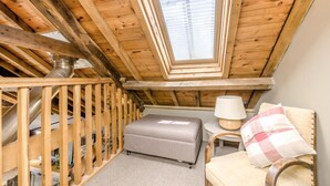 Et lille, hyggeligt soveværelse på loftet med skråvægge, et vindue, en sofa, en lampe og en stol.