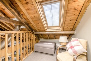 Ein kleines, gemütliches Schlafzimmer im Dachgeschoss mit schrägen Wänden, einem Fenster, einer Couch, einer Lampe und einem Sessel.