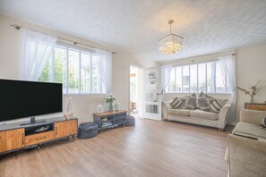 Ein geräumiges Wohnzimmer mit Flachbildfernseher, einer Couch, einem Couchtisch und einer Chandelüster.