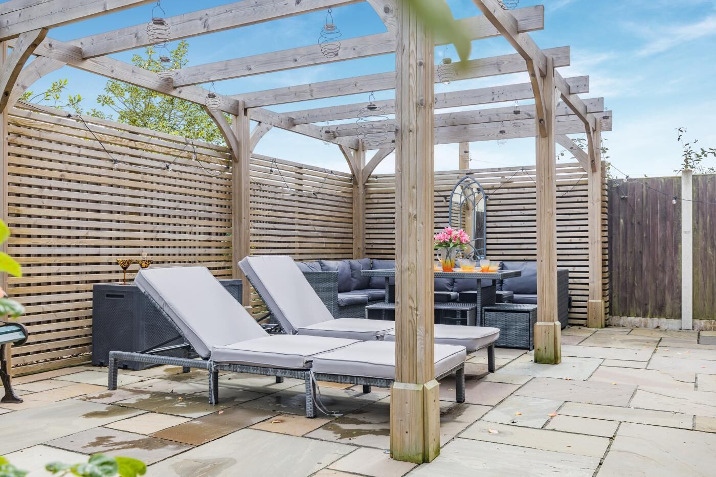 Een overdekt terras met lounge fauteuils en een tafel, omringd door houten latten en een houten schutting.