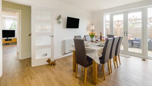 A dining area with a table set for four, a television on the wall, and a view through the glass door to the outside. - 3 Bed in Sheringham (oc-s44832) (Sheringham)