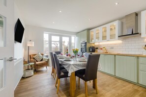 A modern kitchen with white cabinets, a dining table set for four, and a large window providing natural light. - 3 Bed in Sheringham (oc-s44832) (Sheringham)