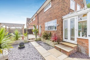 Ein Backsteinhaus mit Terrasse, Garten und überdachter Sitzgelegenheit.