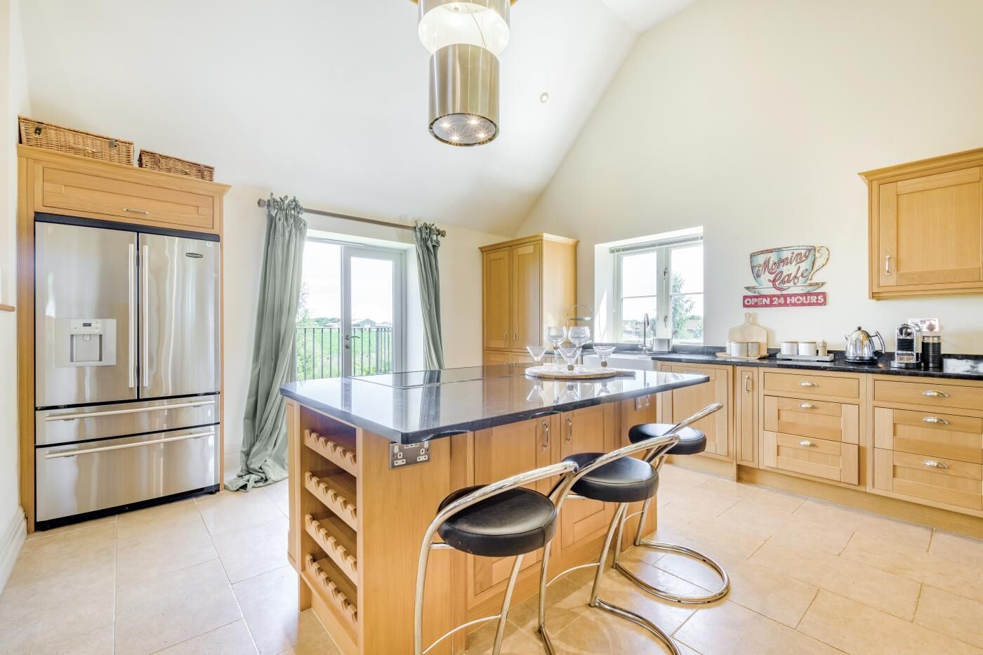 A modern kitchen with a central island, bar stools, stainless steel appliances, and a breakfast bar.