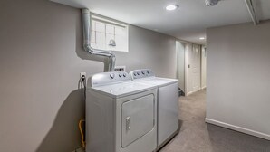 Una sala de lavandería con lavadora y secadora apiladas, un conducto de ventilación y un pasillo que conduce a una puerta.