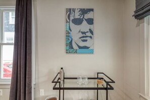 A room with a window, a metal stand with glasses, and a wall-mounted artwork.