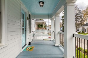 A porch with a swing, a door, and a small rug.