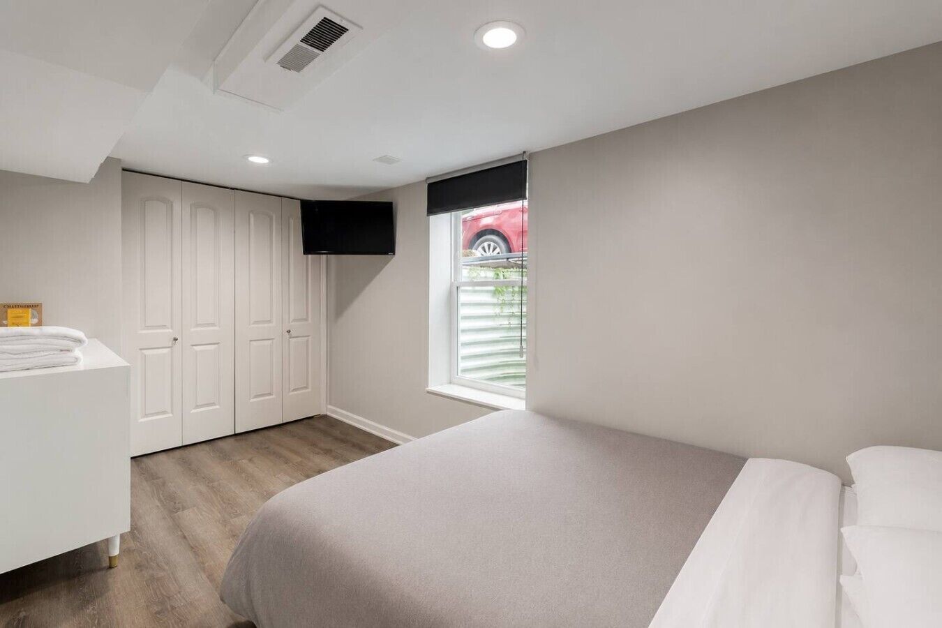 Een slaapkamer met een bed, een witte inbouwkast, een raam met zonwering en een klein tafeltje met handdoeken.