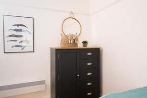 Ein Zimmer mit einem schwarzen Schrank, einem Bilderrahmen mit Walen, einem runden Spiegel und einer kleinen Pflanze.