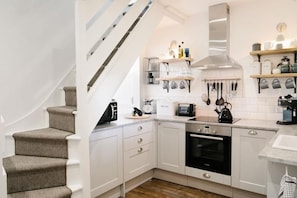 A kitchen with white cabinets, a stove, a sink, and a staircase. - 2 Bed in Mousehole (oc-b584374) (Mousehole)
