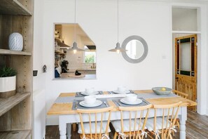 A dining area with a wooden table set for four, white chairs, and a modern pendant light. - 2 Bed in Mousehole (oc-b584374) (Mousehole)