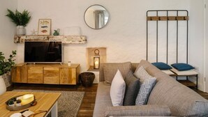 En stue med et tv-skab i træ, en sofa, et lille bord med et lys og et spejl på væggen.