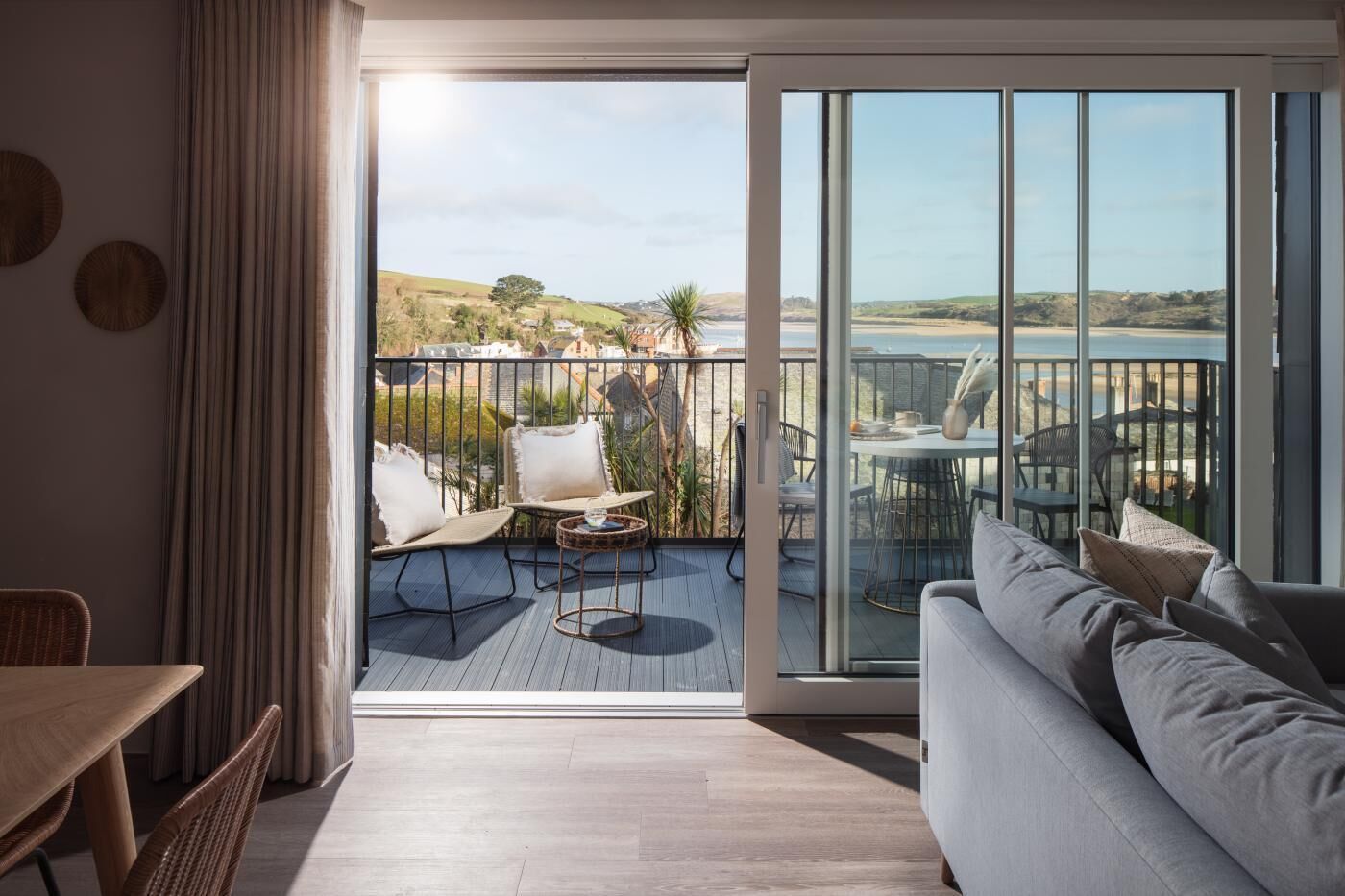 A modern living room with a balcony, a sofa, a dining table, and a view of the beach.