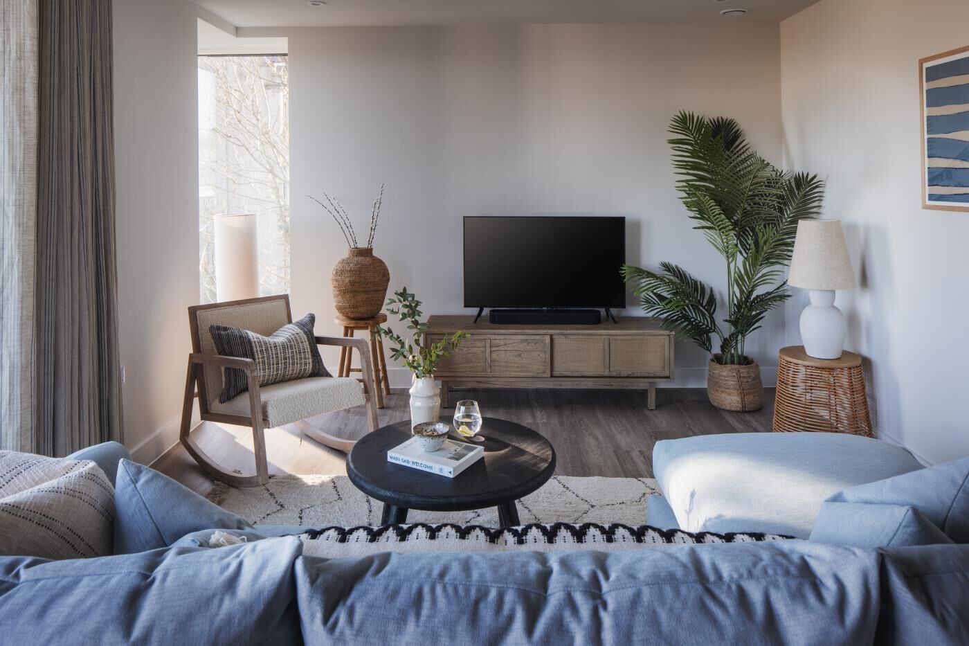 A modern living room with a sofa, armchair, coffee table, TV, and decorative plants.