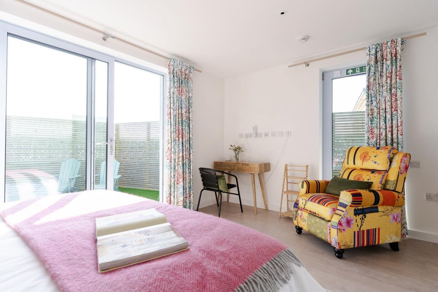 A bedroom with a bed, a desk, a chair, and a balcony with a view.