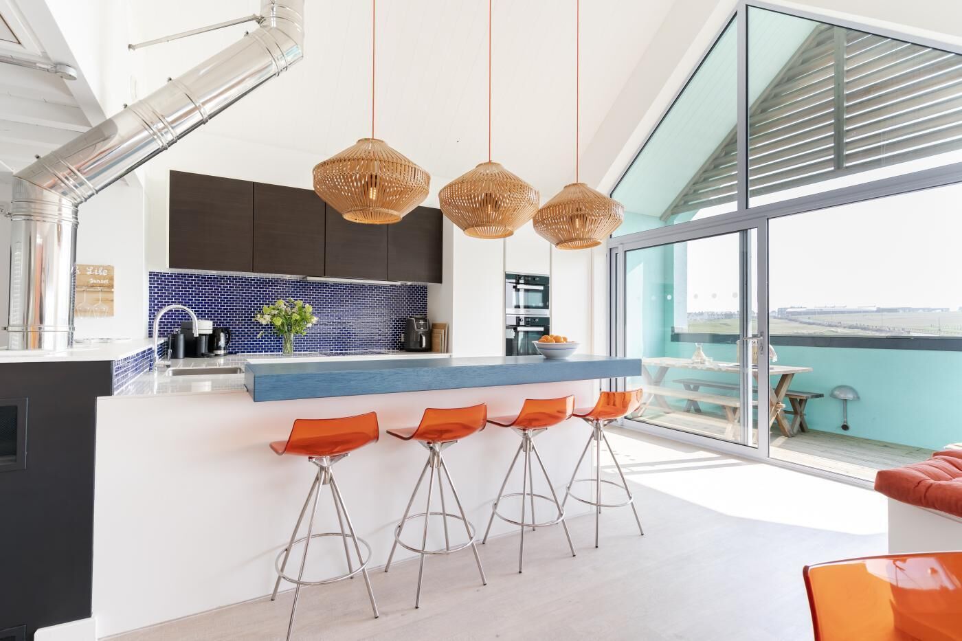 A modern kitchen with a blue backsplash, a central island with bar stools, and a large window offering a view.