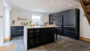 A modern kitchen with a central island, dark cabinetry, and a window providing natural light. - 4 Bed in Porth (oc-b584401) (Newquay)
