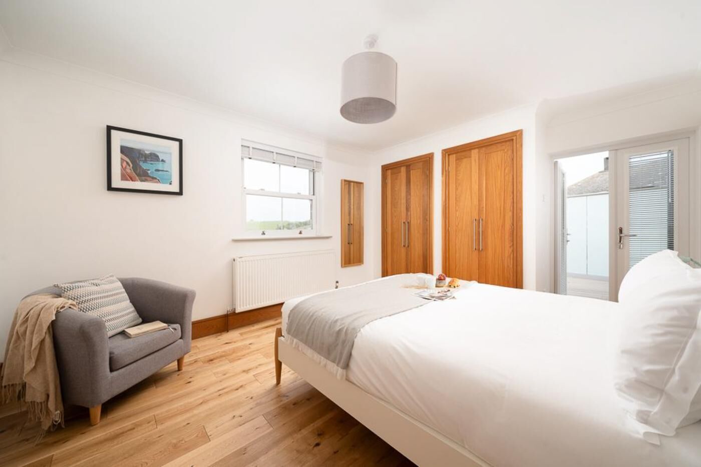 A bedroom with a bed, a grey sofa, wooden wardrobes, a radiator, and a window.