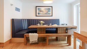 A modern dining area with a wooden table, bench seating, and a framed artwork above. - 4 Bed in Porth (oc-b584401) (Newquay)