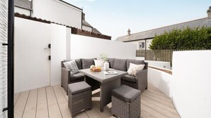 A patio with a grey sofa set, a small table, and a wicker ottoman. - 4 Bed in Porth (oc-b584401) (Newquay)