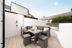 Eine Terrasse mit einer grauen Sofagarnitur, einem kleinen Tisch und einem Korbsitzhocker.