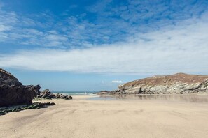 Una platja amb cel clar, penya-segats rocosos i una riba sorrenca.