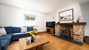A living room with a sofa, a coffee table with a vase of sunflowers, a fireplace, and a television. - 4 Bed in Porth (oc-b584401) (Newquay)