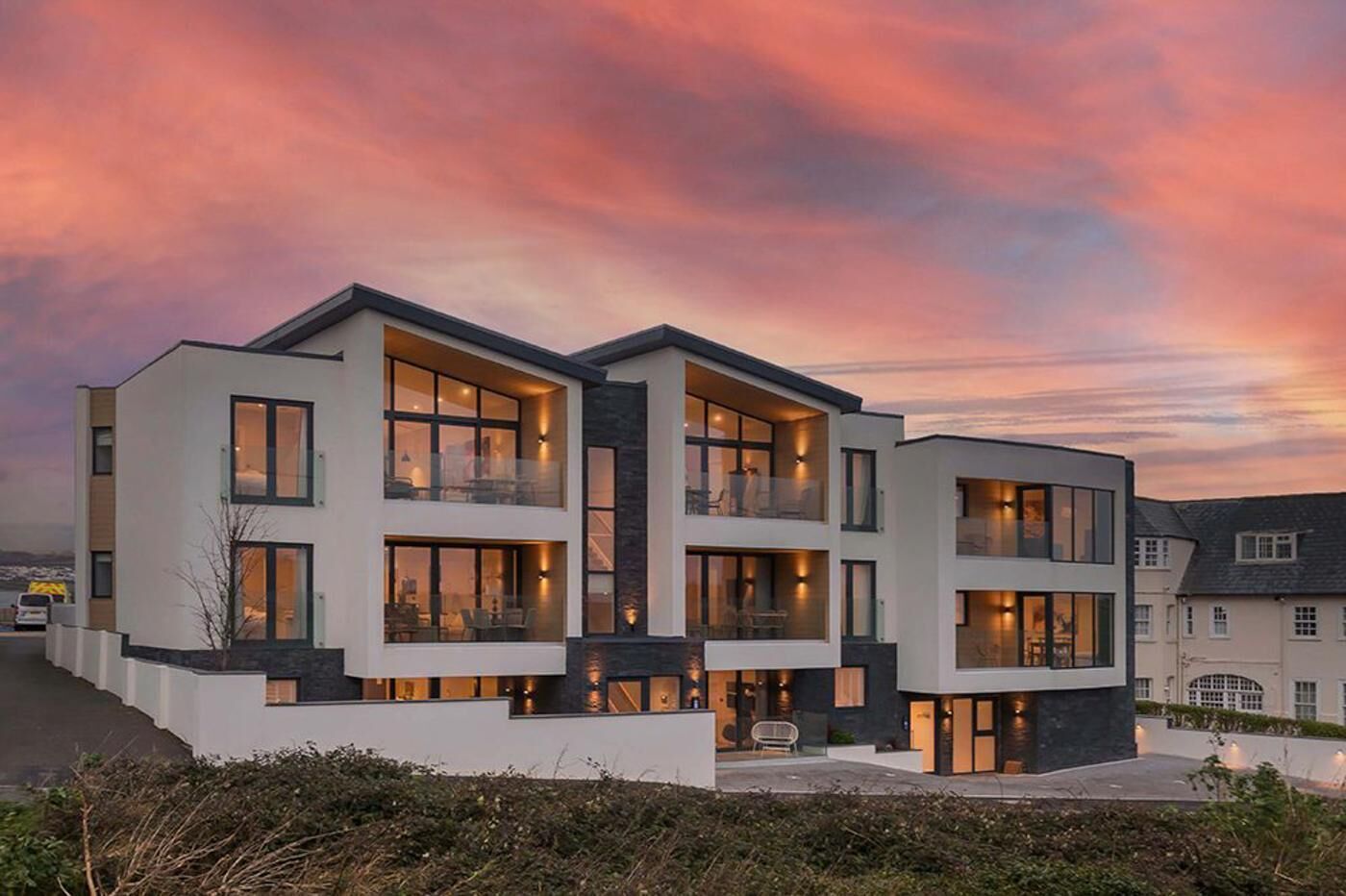 A modern two-story residential building with balconies, large windows, and a well-lit facade.