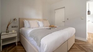 Et soveværelse med seng, natbord, lampe og en dør.
