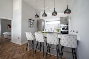 A modern kitchen with a central island, bar stools, pendant lighting, and a visible window. - 2 Bed in Bude (oc-b588790) (Bude)