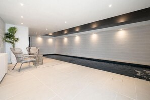 A modern indoor pool area with a seating area, a potted plant, and a wall with recessed lighting. - 2 Bed in Bude (oc-b588790) (Bude)