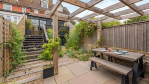 A covered patio with a wooden table and benches, surrounded by a garden and a wooden fence. - 2 Bed in Rye (oc-s43273) (Rye Harbour)