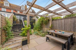 A covered patio with a wooden table and benches, surrounded by a garden and a wooden fence. - 2 Bed in Rye (oc-s43273) (Rye Harbour)