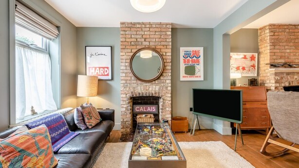 A living room with a brick fireplace, a sofa, a coffee table with board games, and a television on a stand. - 2 Bed in Rye (oc-s43273) (Rye Harbour)