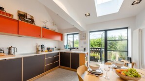 A modern kitchen with a dining area, featuring a large window and a view of greenery outside. - 2 Bed in Rye (oc-s43273) (Rye Harbour)