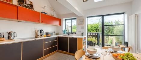 A modern kitchen with a dining area, featuring a large window and a view of greenery outside.