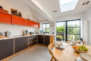 A modern kitchen with a dining area, featuring a large window and a view of greenery outside. - 2 Bed in Rye (oc-s43273) (Rye Harbour)