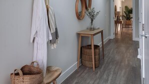 A hallway with a wooden floor, a small wooden table with a vase, and a hanging coat rack. - 2 Bed in Padstow (oc-b623759) (Padstow)