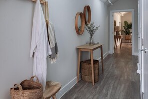 A hallway with a wooden floor, a small wooden table with a vase, and a hanging coat rack. - 2 Bed in Padstow (oc-b623759) (Padstow)