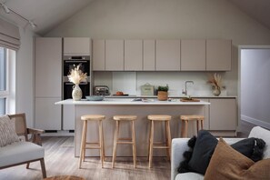 A modern kitchen with a central island, bar stools, and a dining area with a sofa. - 2 Bed in Padstow (oc-b623759) (Padstow)