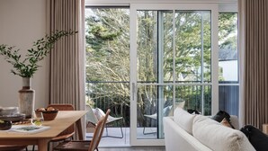 A modern living room with a sofa, dining table, and chairs, a large sliding glass door leading to a balcony with outdoor furniture. - 2 Bed in Padstow (oc-b623759) (Padstow)