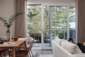 A modern living room with a sofa, dining table, and chairs, a large sliding glass door leading to a balcony with outdoor furniture. - 2 Bed in Padstow (oc-b623759) (Padstow)