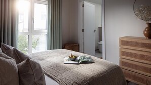 A bedroom with a bed, a bedside table with a vase, and a view of a bathroom through an open door. - 2 Bed in Padstow (oc-b623759) (Padstow)