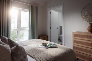 A bedroom with a bed, a bedside table with a vase, and a view of a bathroom through an open door. - 2 Bed in Padstow (oc-b623759) (Padstow)