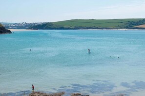 A coastal scene with calm waters, a person paddleboarding, and a distant shoreline with buildings. - 2 Bed in Padstow (oc-b623759) (Padstow)