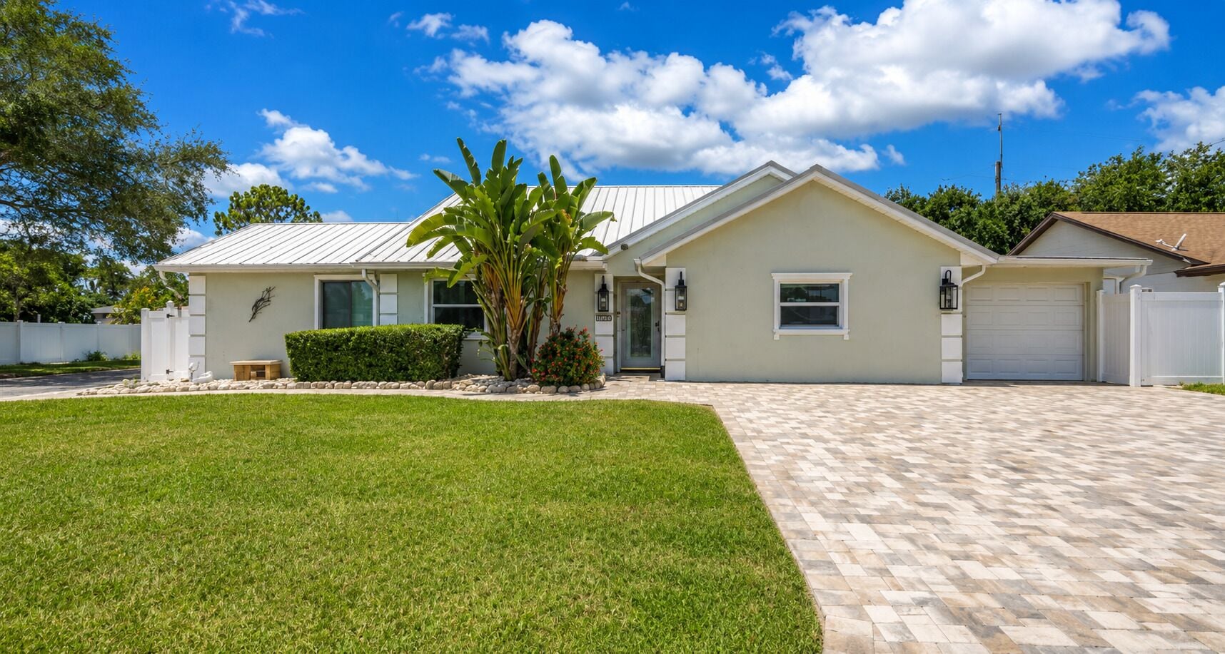 A single-story house with a front lawn, a garage, and a small garden with a palm tree.