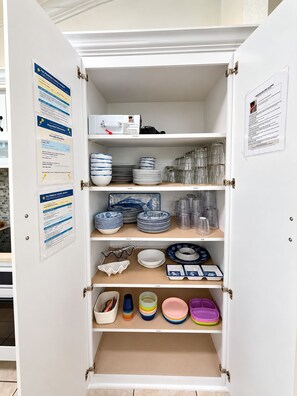 A storage cabinet with multiple shelves containing various kitchenware items. - The Primrose Coastal Retreat •Private Heated Pool • Near Anna Maria Island (Bradenton)