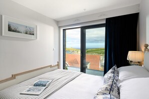 A hotel room with a bed, a window with a view of the countryside, a bedside table with a lamp, and a framed picture on the wall. - 2 Bed in Porth (oc-b642115) (Newquay)