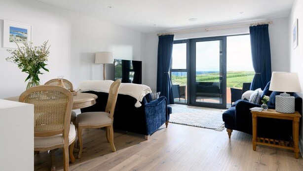 Een moderne kamer met een eethoek, een zithoek, een televisie en een grote schuifpui naar een balkon met uitzicht.